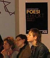 Detalj ur den större bilden: publik framför en svart affisch med texten POESI