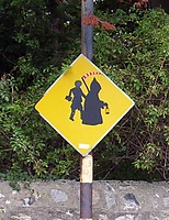 irländsk vägskylt med två figurer som bär på lykta, lie och något fyrkantigt